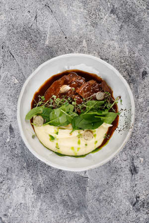Veal cheeks in gravy with potatoes and cabbage, decorated with herbs on a white plateの写真素材