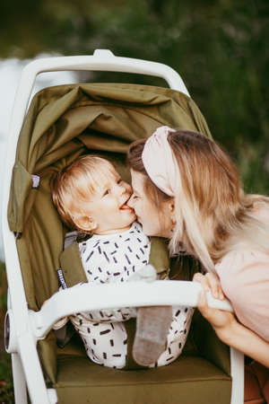 Happy young mother with baby in buggy walking in park