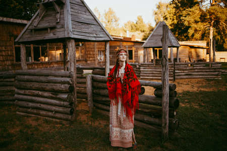 A beautiful Slavic girl with long blonde hair and brown eyes in a white and red embroidered suit is...