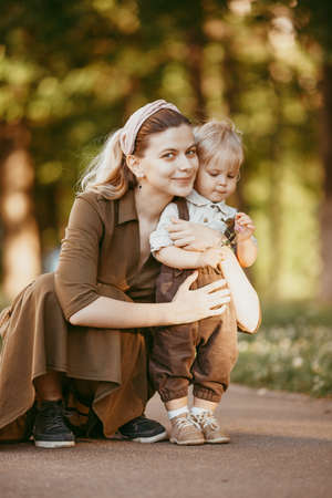 A young mother helps her son start walking. A mother teaches her son, educates him, and takes care of him.summer dayの写真素材