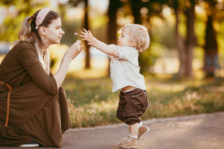 A young mother helps her son start walking. A mother teaches her son, educates him, and takes care of him.summer dayの写真素材