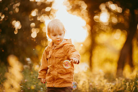 Cute baby boy walking in the beige jacket at sunset, on an autumn day