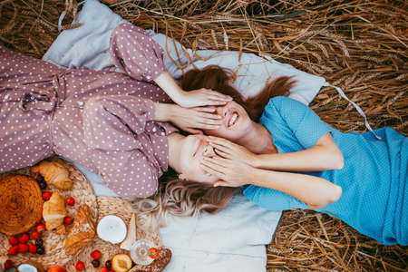 happy friends in a wheat field. girls on a picnic in a field near wheat ears at sunset.の写真素材