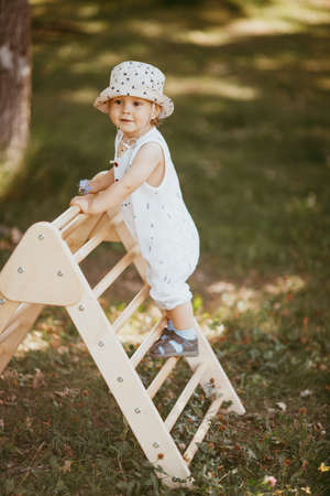 Cute boy performs gymnastic exercises on a wooden home sports complex stairs. Children's sports exercises. Physical education of childrenの写真素材