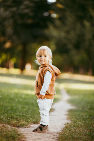 a boy in a brown vest with a hood walks through the autumn forest in the eveningの写真素材