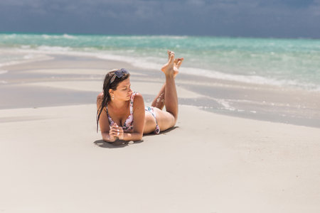 A young woman in a bikini swimsuit looks into the distance at a sandy beach.の写真素材
