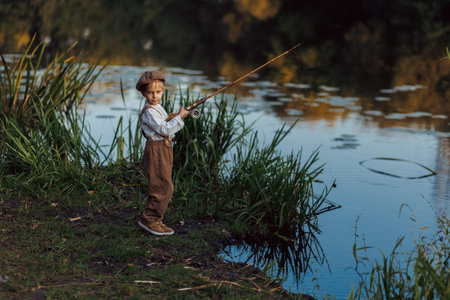 Little boy is fishing at sunset on the lakeの写真素材