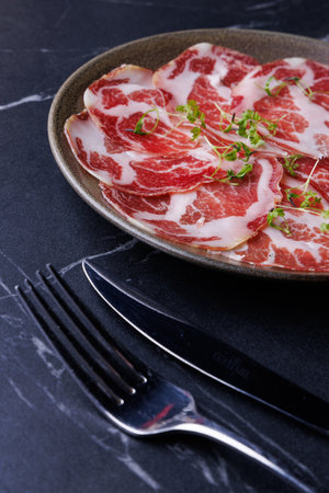 Plate of Marbled Raw Meat Slices Garnished with Fresh Herbsの写真素材