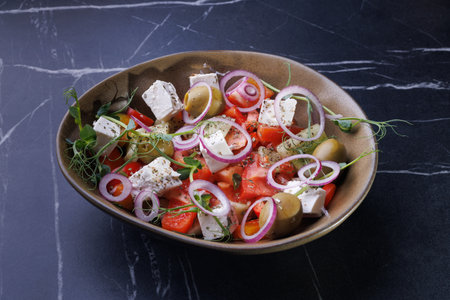 Fresh Greek Salad Bowl With Feta, Olives, Red Onion, And Herb Garnish On Dark Marbleの写真素材
