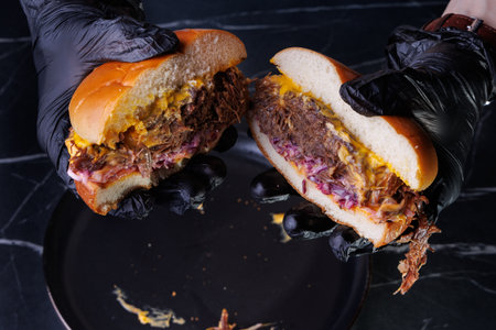 Close-up of hands in black gloves assembling a burger with cheese and a sesame bun on a metal tray, highlighting fresh ingredients. Perfect for food preparation, culinary arts, and restaurant themes.の写真素材