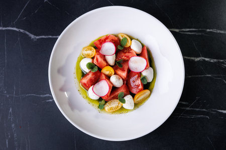 Colorful Tomato Burrata Salad With Radish, Olives, And Fresh Herbs On White Plateの写真素材