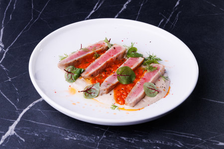 Seared Tuna Steak Slices on Creamy Sauce with Fresh Greens and Herbsの写真素材