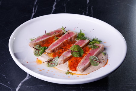 Seared Tuna Steak Slices on Creamy Sauce with Fresh Greens and Herbsの写真素材