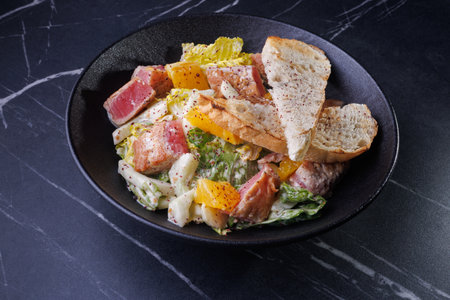 Creamy Bacon Salad With Oranges, Croutons, And Fresh Greens In A Black Bowlの写真素材