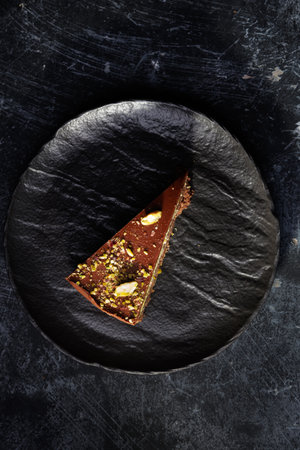 Rich Chocolate Cake Slice With Pistachio Cream Layer And Nut Crumble On Dark Plateの写真素材