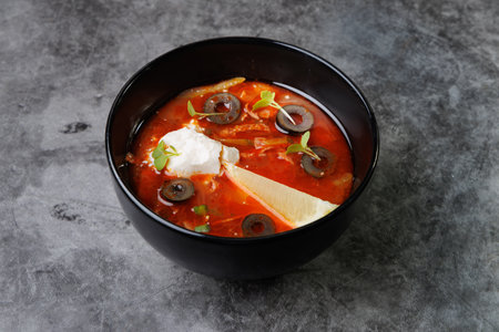 Red Tomato Soup In Black Bowl With Olive Slices, And Fresh Microgreens