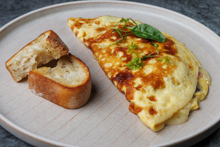 A warm breakfast setting featuring a golden cheese omelette garnished with greens, a slice of crusty...