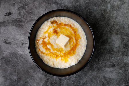 A black bowl holds creamy porridge topped with a pat of butter and ribbons of honey. Simple, comforting breakfast for a peaceful morning at home.の写真素材