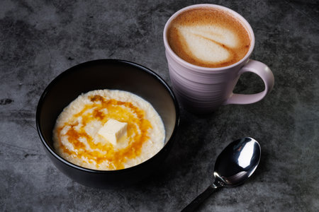 A comforting morning scene with creamy oatmeal topped with butter and syrup, paired with a frothy coffee in a soft pink mug. Cozy, simple breakfast imagery perfect for lifestyle and food collections.の写真素材