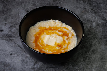A black bowl holds creamy porridge topped with a pat of butter and ribbons of honey. Simple, comforting breakfast for a peaceful morning at home.の写真素材