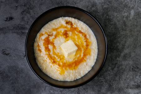 A black bowl holds creamy porridge topped with a pat of butter and ribbons of honey. Simple, comforting breakfast for a peaceful morning at home.の写真素材