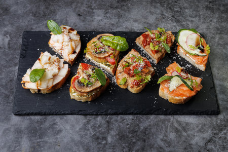 A selection of bite-sized canap s featuring salmon, vegetables, and fresh herbs arranged on a dark slate tray. Perfect for catering, parties, and stylish appetizer spreads vibrant colors, textures, and gourmet flavors.の写真素材