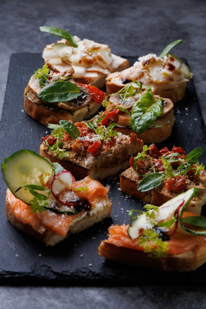 A selection of bite-sized canap s featuring salmon, vegetables, and fresh herbs arranged on a dark...