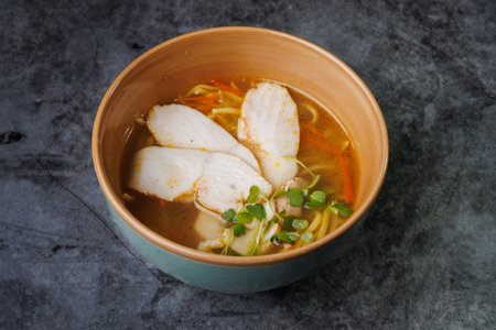 A comforting bowl of chicken noodle soup featuring sliced chicken, tender noodles, carrot ribbons, and fresh microgreens in a rich broth. Perfect for cozy meals, family dinners, and everyday kitchen scenes.の写真素材