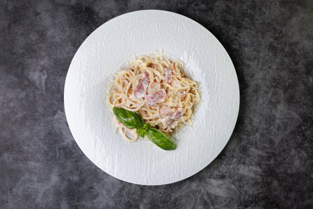 A creamy carbonara pasta dish featuring bacon bits and fresh basil on a clean white plate, showing classic Italian flavors and a comforting, gourmet presentation.の写真素材
