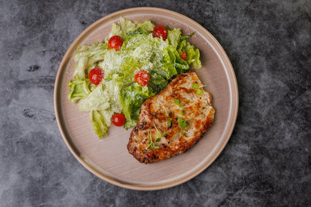Juicy grilled chicken beside a crisp romaine salad with cherry tomatoes on a soft beige plate. Fresh greens, light dressing, and herbs create a healthy, appealing dinner scene.の写真素材