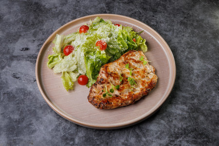 Juicy grilled chicken beside a crisp romaine salad with cherry tomatoes on a soft beige plate. Fresh greens, light dressing, and herbs create a healthy, appealing dinner scene.の写真素材