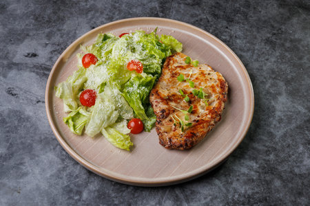 Juicy grilled chicken beside a crisp romaine salad with cherry tomatoes on a soft beige plate. Fresh greens, light dressing, and herbs create a healthy, appealing dinner scene.の写真素材