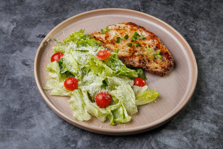 Juicy grilled chicken beside a crisp romaine salad with cherry tomatoes on a soft beige plate. Fresh greens, light dressing, and herbs create a healthy, appealing dinner scene.の写真素材