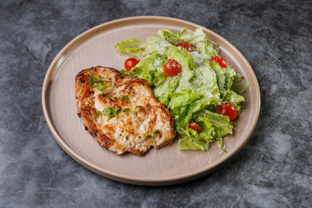 Juicy grilled chicken beside a crisp romaine salad with cherry tomatoes on a soft beige plate. Fresh greens, light dressing, and herbs create a healthy, appealing dinner scene.の写真素材