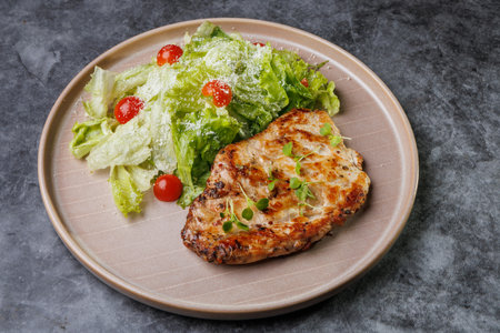 Juicy grilled chicken beside a crisp romaine salad with cherry tomatoes on a soft beige plate. Fresh greens, light dressing, and herbs create a healthy, appealing dinner scene.の写真素材
