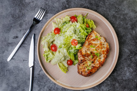 Juicy grilled chicken beside a crisp romaine salad with cherry tomatoes on a soft beige plate. Fresh greens, light dressing, and herbs create a healthy, appealing dinner scene.の写真素材