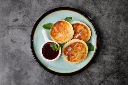 Golden-crusted pancakes served on a white plate with berry sauce and fresh mint create a warm and cozy atmosphere for breakfast or dessert, perfect for cooking, cafes, and home cooking.の写真素材