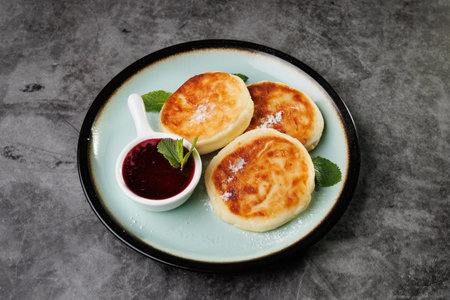 Golden-crusted pancakes served on a white plate with berry sauce and fresh mint create a warm and cozy atmosphere for breakfast or dessert, perfect for cooking, cafes, and home cooking.の写真素材
