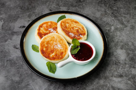 Golden-crusted pancakes served on a white plate with berry sauce and fresh mint create a warm and cozy atmosphere for breakfast or dessert, perfect for cooking, cafes, and home cooking.の写真素材