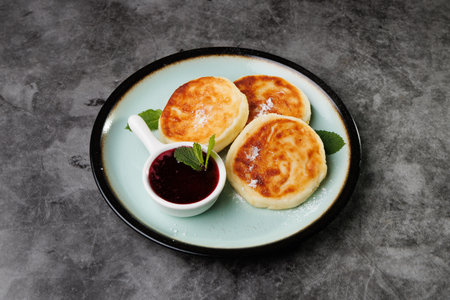 Golden-crusted pancakes served on a white plate with berry sauce and fresh mint create a warm and cozy atmosphere for breakfast or dessert, perfect for cooking, cafes, and home cooking.の写真素材