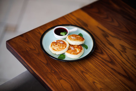A close-up of three pan-fried dumplings arranged on a light blue plate, accompanied by a small spoon of berry sauce and fresh mint leaves. Natural indoor lighting with a leafy plant in the background.の写真素材