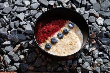 A nourishing bowl of oats topped with blueberries and a splash of red berry powder, presented on a dark ceramic plate to evoke a cozy, healthy breakfast mood.の写真素材