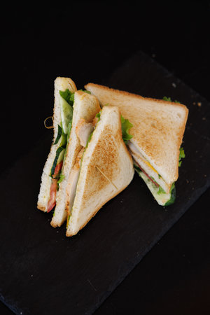 A toasted sandwich layered with crisp lettuce, tomato, cheese, and ham rests on a dark slate...