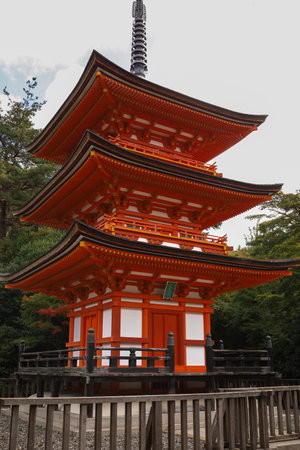 Vibrant orange-red pagoda stands amid lush trees in a tranquil Japanese temple park. Architecture highlights curved roofs, wooden beams, and a tall spire, offering a serene cultural scene for travel and heritage themes.の写真素材