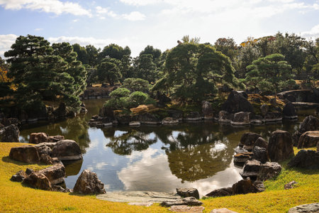 A peaceful garden pond featuring large rocks, calm water reflections, and surrounding trees. Ideal for serene, nature, landscape, and Zen-inspired stock imagery.の写真素材