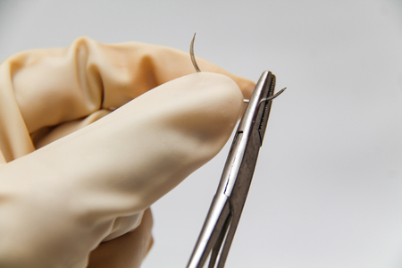 Holding a surgery needle (straight 1/2 circle) with needle holder and hand glovesの写真素材
