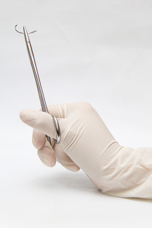 Holding a surgery needle (straight 1/2 circle) with needle holder and hand glovesの写真素材