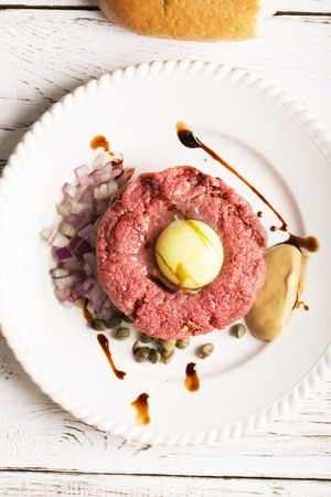 tartare with egg yolk, onions and capers closeup on a white plateの写真素材