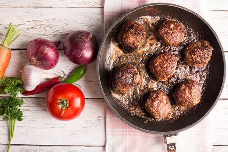 Fried meatballs on the pan and vegetables on the wooden tableの写真素材
