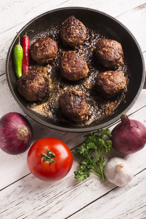 Fried meatballs on the pan and vegetables on the wooden tableの写真素材